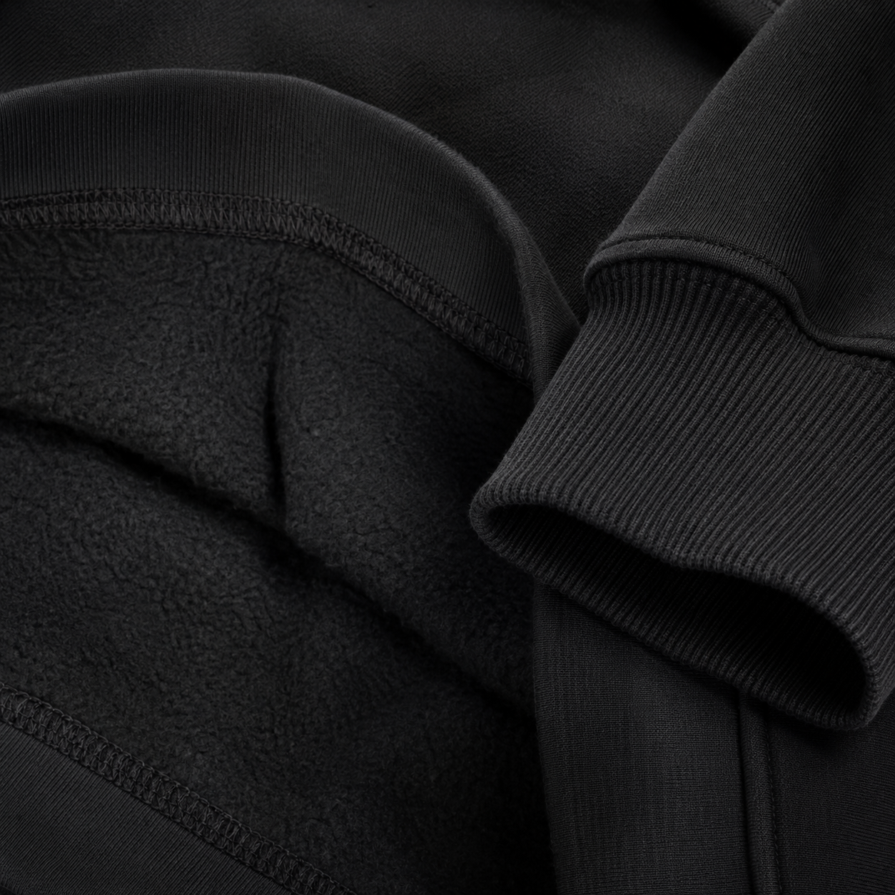 Macro close-up of a premium hoodie showing reinforced interior seam stitching, ribbed cuff construction, and soft brushed fleece lining.